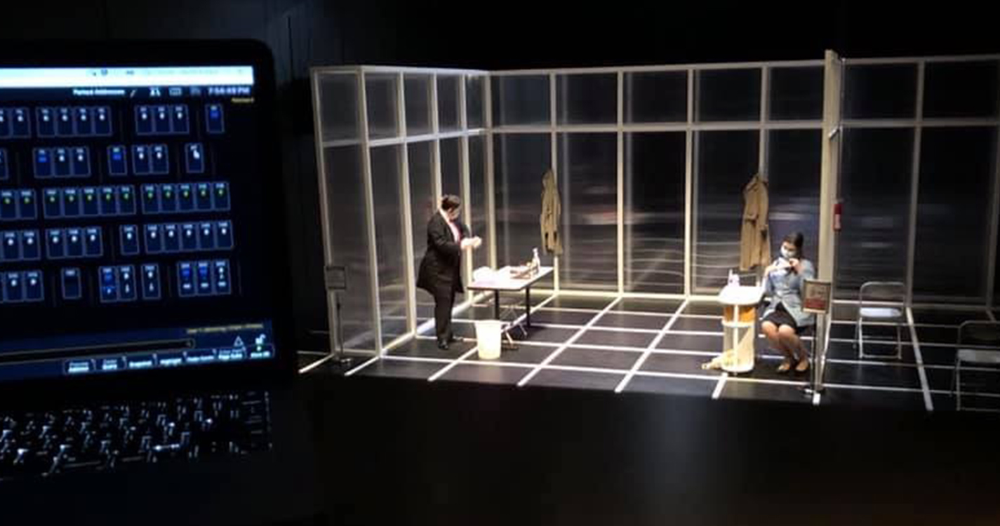 two actors wear masks on a black stage set marked with a white grid