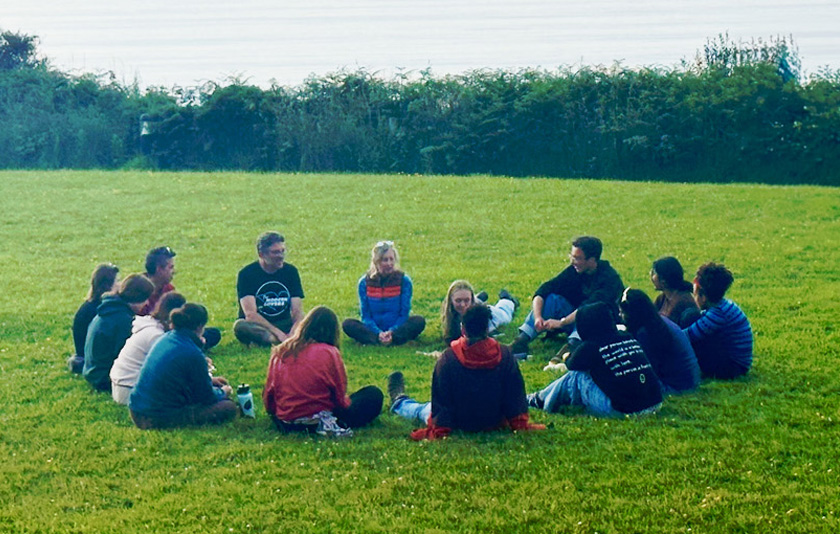 Students and faculty sitting in a circle in a grassy field