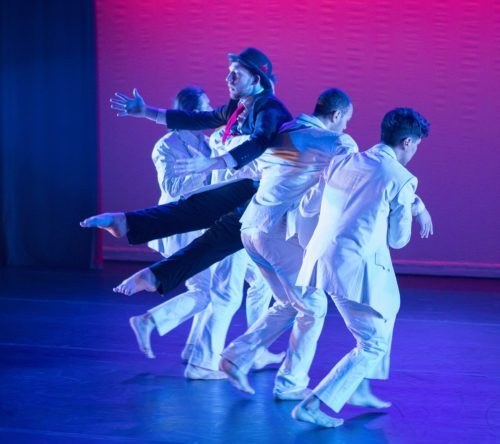 Three dancers in white suits holding a dancer in a black suit and hat