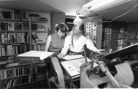 Two people examining a newspaper spread on a printing machine