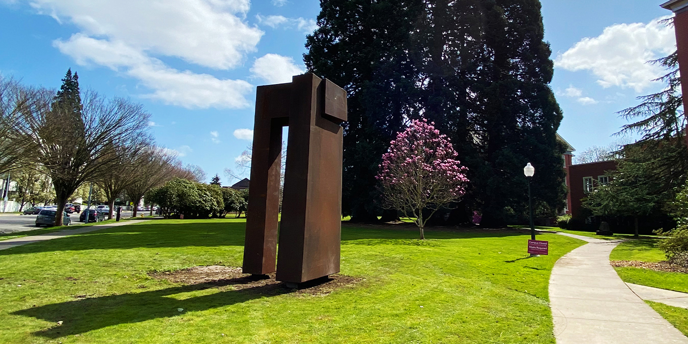 rust colored geometric metal sculpture cast a shadow on green grass