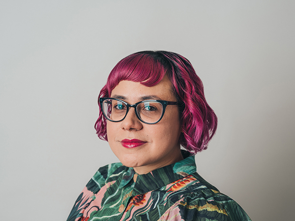 Young Woman with red hair smiling wearing glasses and a green multi-colored blouse